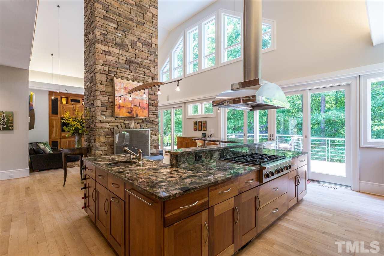 A large multi-level U-shaped island with Brazilian Verde Marinace granite counter includes a lower wing w/stainless-steel vegetable prep sink, a long section with a gas stove and work surfaces backing up to a higher serving counter.