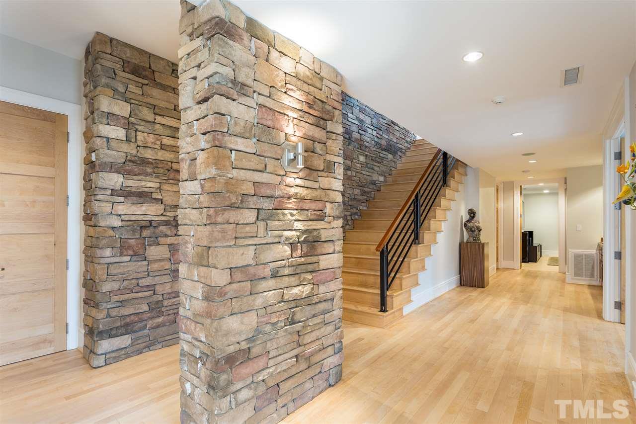 The wide lower-level hallway has white maple hardwood flooring and a stone wall illuminated by modern sconces and recessed lighting.  A well-appointed wet-bar is open to the hallway and is located between the gym and media room.