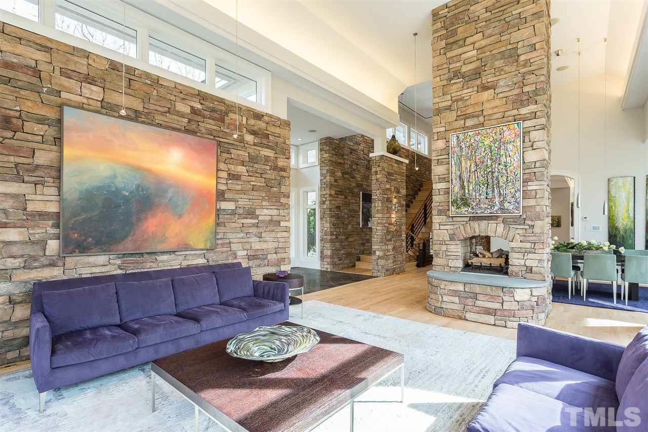 The living room offers 20 ft. ceilings, cove-light molding, dimmable recessed lighting, art spotlights, automated shades, a full wall of warm stone, and a masonry floor-to-ceiling double-sided fireplace with gas logs and slate hearth.