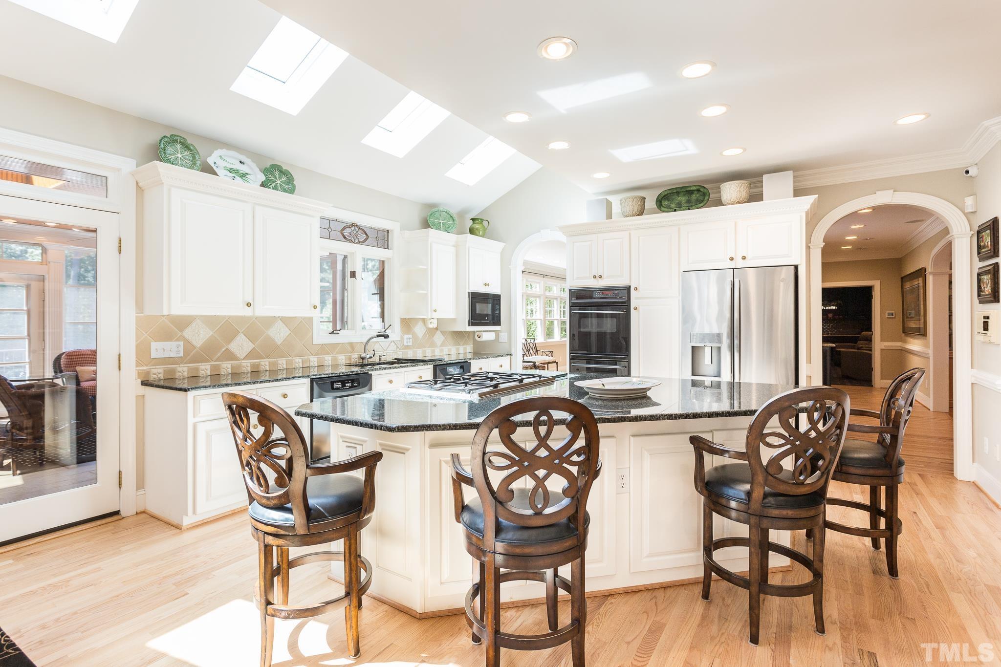 The open kitchen is illuminated by a full row of skylights.and features  a large central island, walk-in pantry, built-in desk, under-cabinet lighting, granite countertops, 6-burner gas cooktop, double ovens, two Kitchen Aid dishwashers
