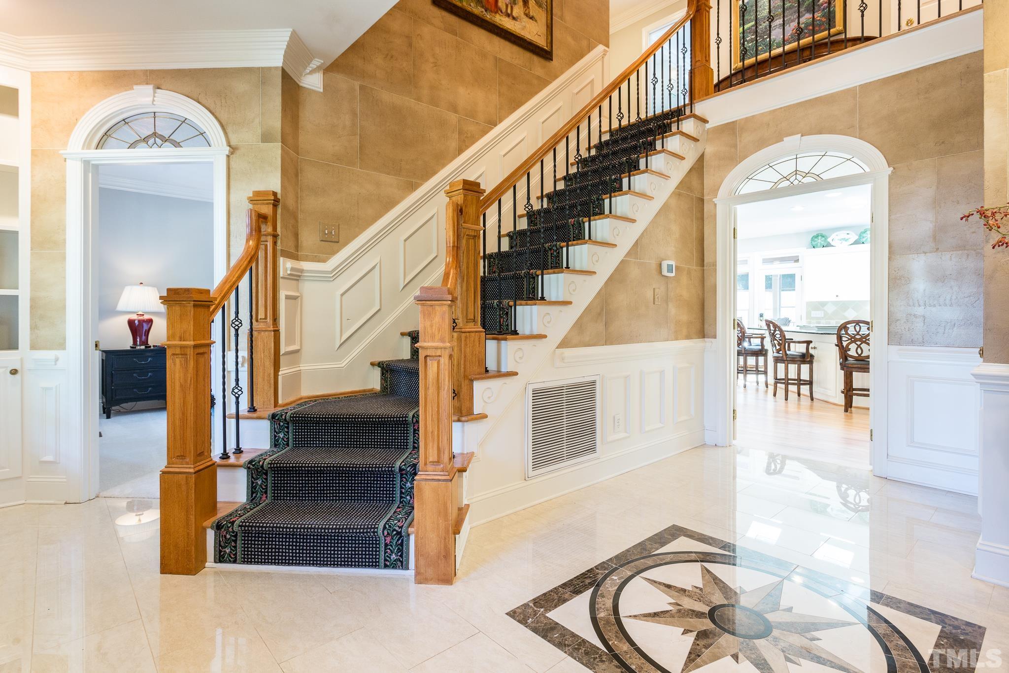 The gracious foyer welcomes you to the home and features a turned staircase, wrought iron spindles, display shelving on either side of the front door, coat closet, faux painted walls, and marble floors with a custom-designed inlay
