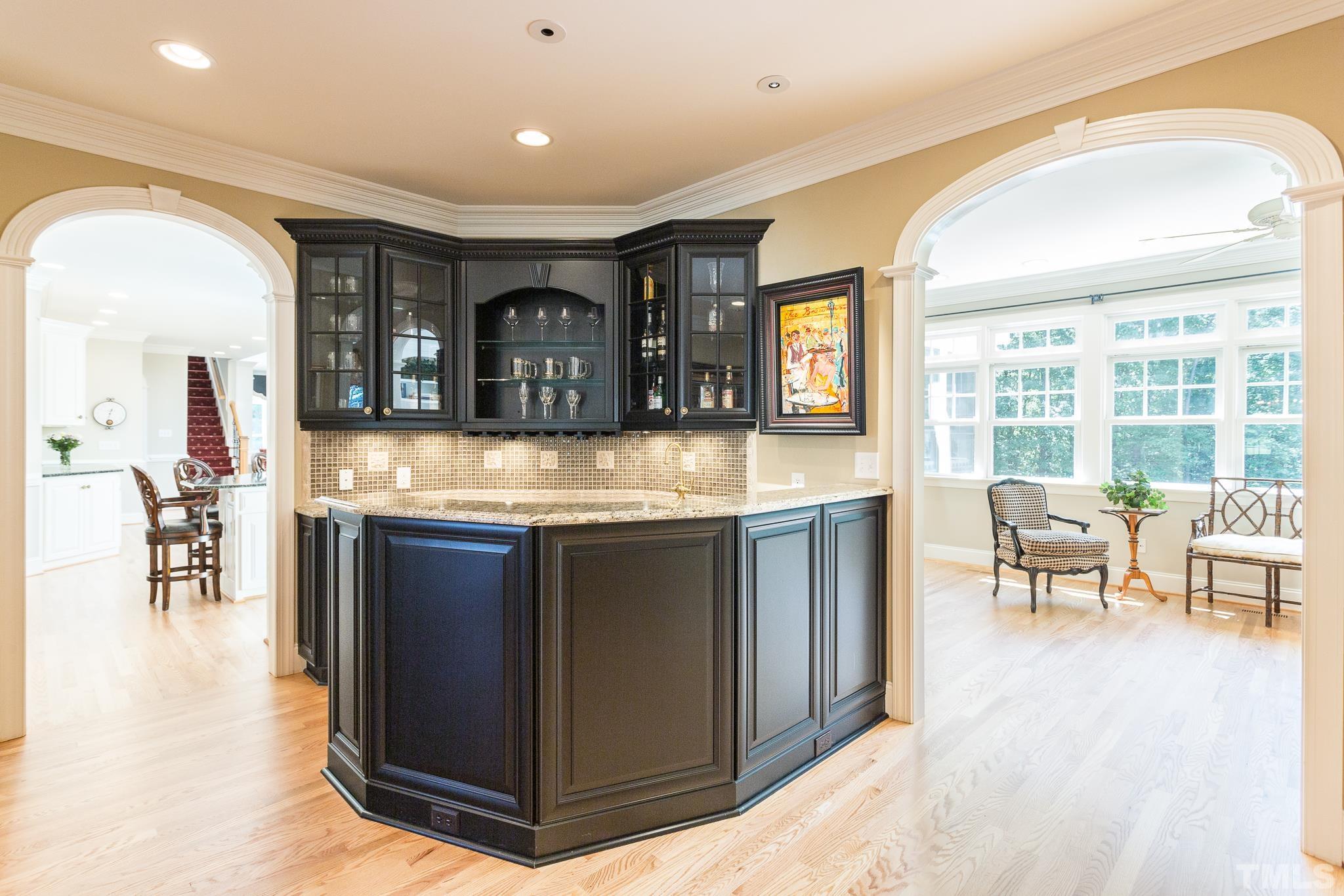 The bar is centrally located between the kitchen, dining room, sunroom and theater room and lends itself to entertaining. It offers glass front cabinets, tile backsplash, granite counters, and a beverage refrigerator