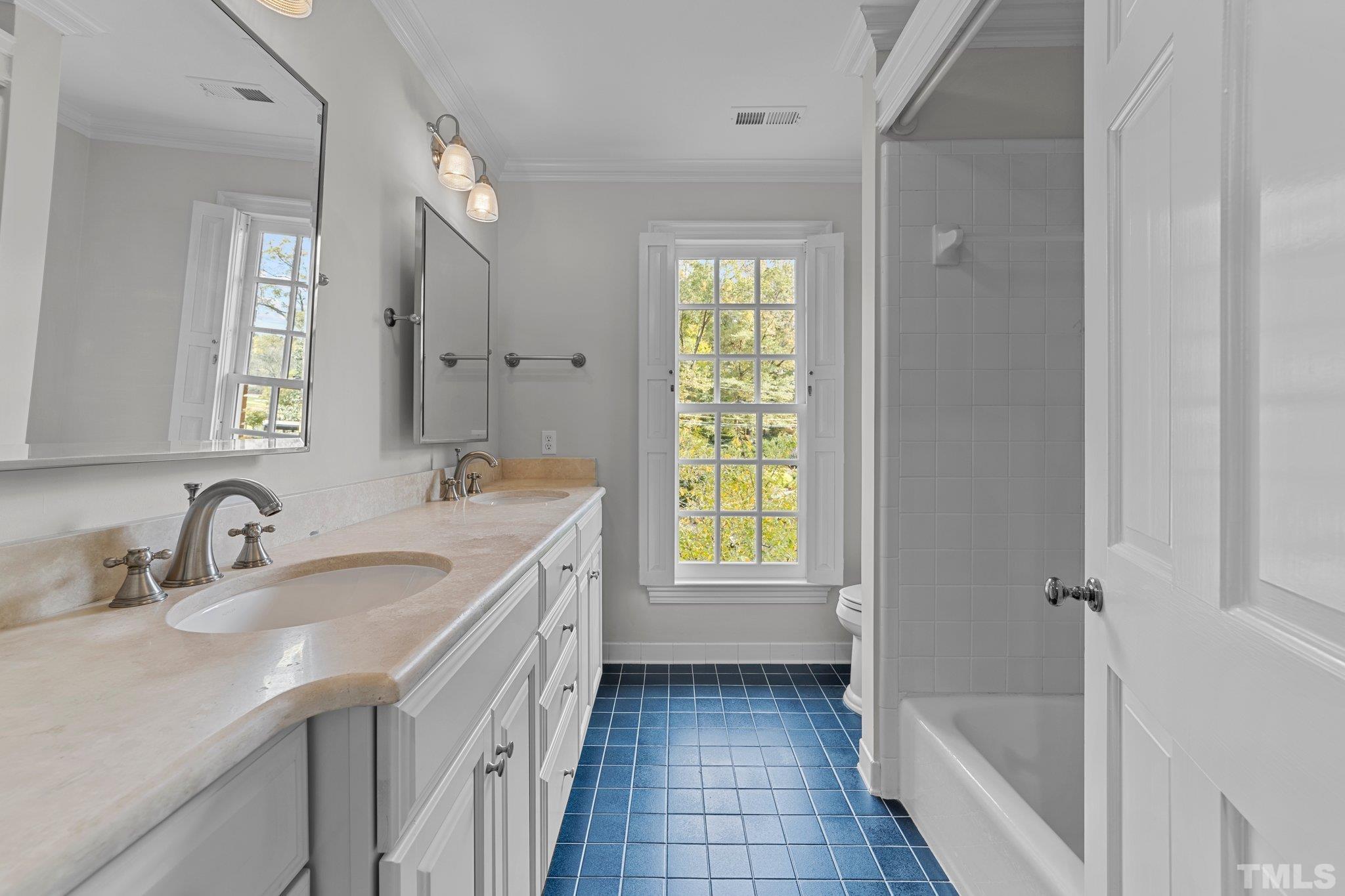 Large hall bath with dual vanities & pretty mirrors, ceramic tub surround with shower and cheerful ceramic floor.