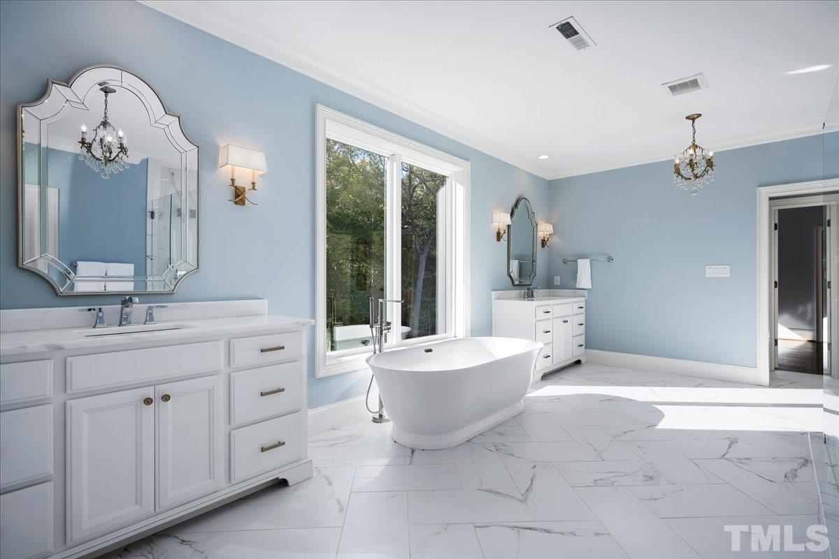 Sprawling master bathroom with stunning, private views. Second doorway opens to massive double laundry room. Double vanities with custom sconces and mirrors. Two walk-in closets with ceiling-to-floor shelving. Water closet with stunning lighting.
