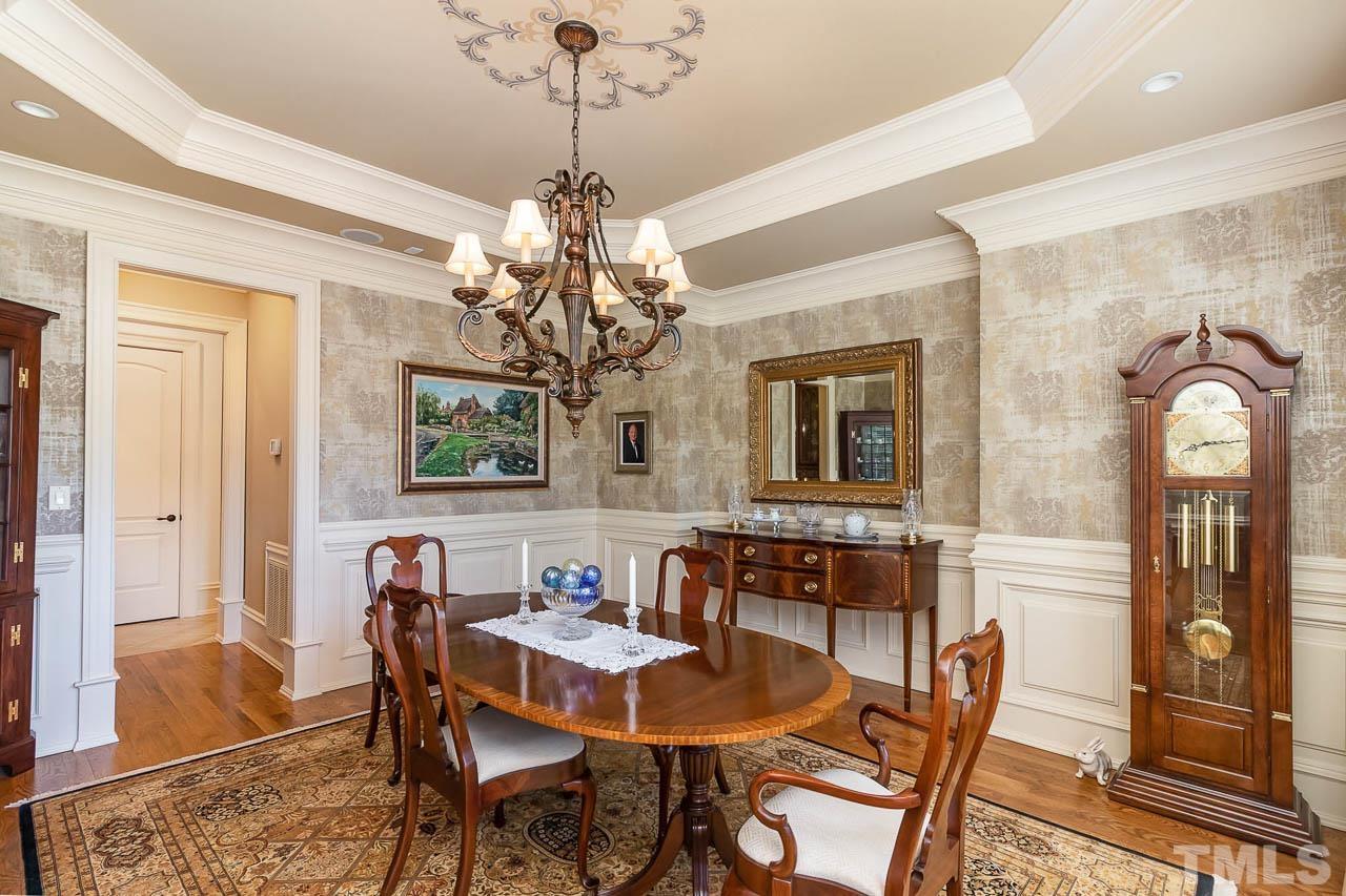 This beautiful dining room has wainscotting panels, a tray ceiling with hand painted embellishments, and a chandelier.