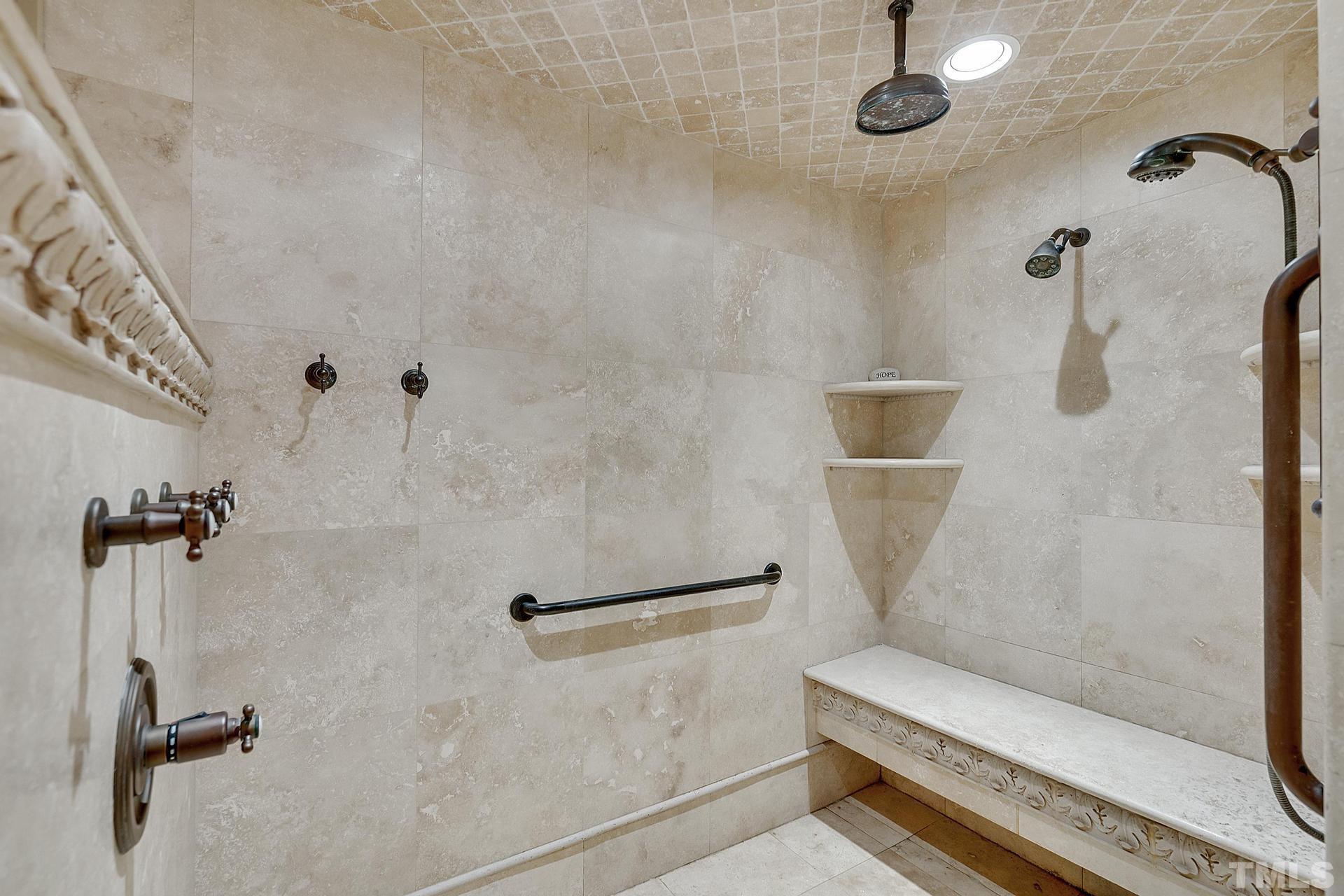 Large walk in shower with three shower heads, built in seats and towel/robe hooks.